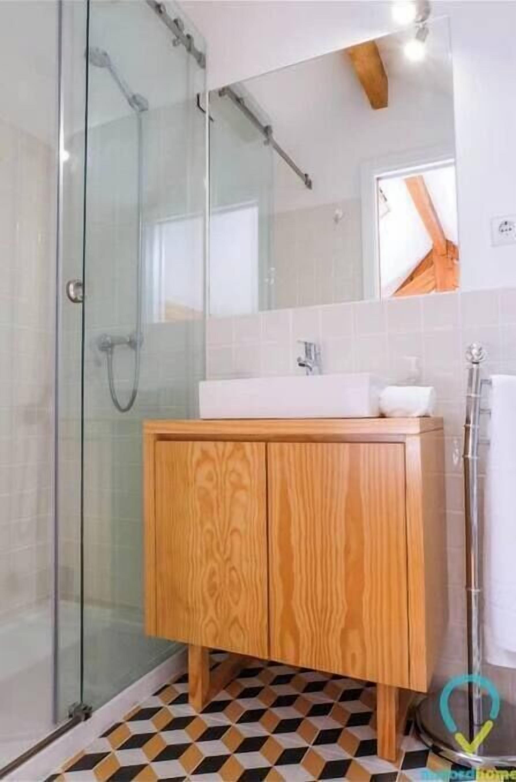 Une salle de bain avec une douche à parois de verre, un meuble-lavabo en bois et un carrelage à motifs à carreaux.