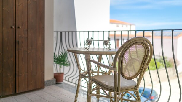 Un balcón con una silla y una mesa de mimbre, una planta en maceta y vistas a edificios.
