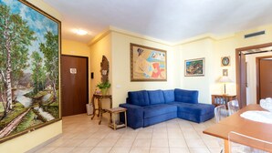 Una sala de estar con un sofá azul, una mesa de comedor, un cuadro y una puerta.