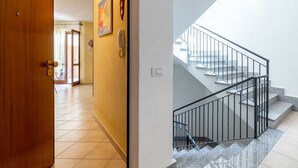 Un pasillo con puerta de madera, un teléfono en la pared y una escalera con barandilla metálica.
