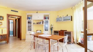 Un comedor con una mesa y sillas de madera, un armario blanco con libros y un televisor en la pared.
