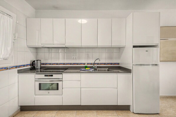 A kitchen with white cabinets, a stainless steel sink, a built-in oven, and a refrigerator.