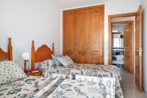 Un dormitorio con dos camas, un armario de madera y una mesita de noche con una lámpara.