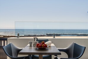 Una mesa con un bol de fruta, una cafetera y tazas, con vista al mar.