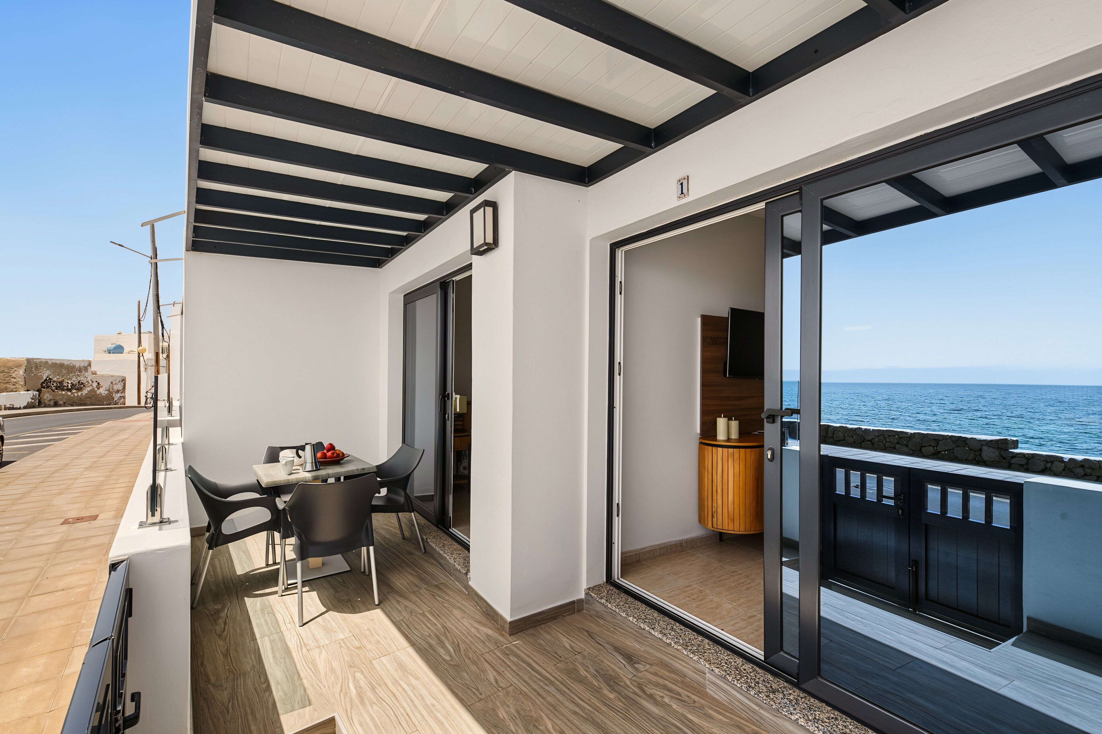 A balcony with a table and chairs, a wooden floor, and a view of the sea.