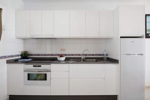Een moderne keuken met witte kasten, een roestvrijstalen spoelbak, een ingebouwde oven en een koelkast.