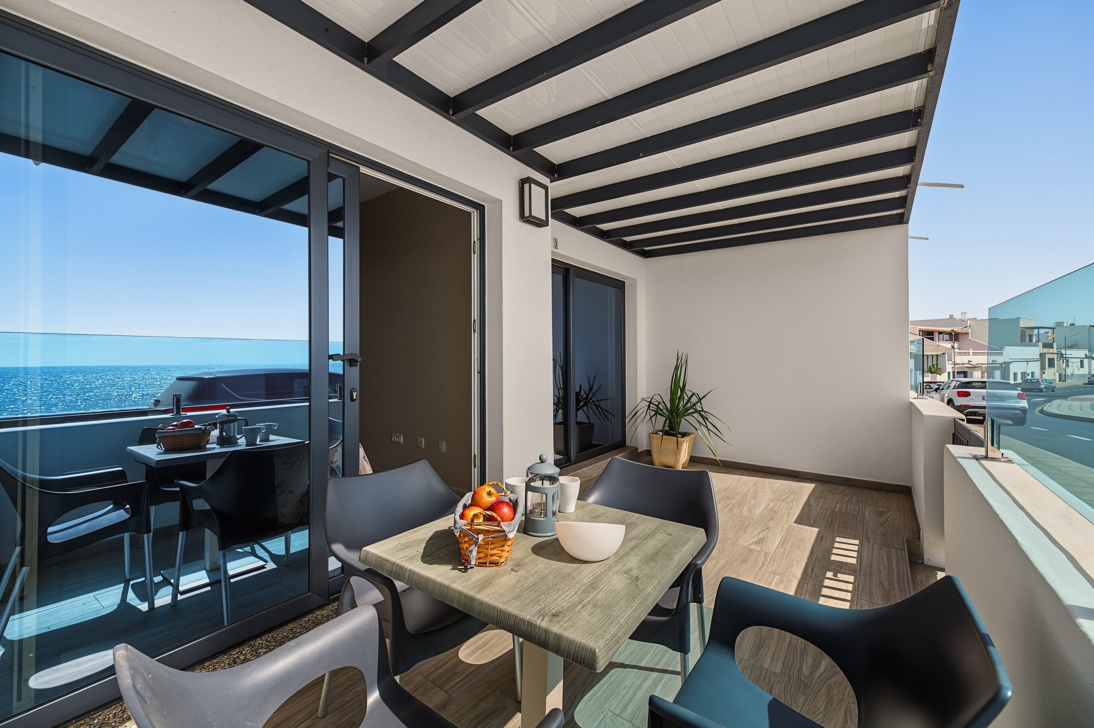 Un balcón con mesa y sillas dispuestas para comer, una planta en maceta y vista al mar.