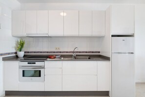 Een moderne keuken met witte kastjes, een inbouwoven, een roestvrijstalen spoelbak en een koelkast.