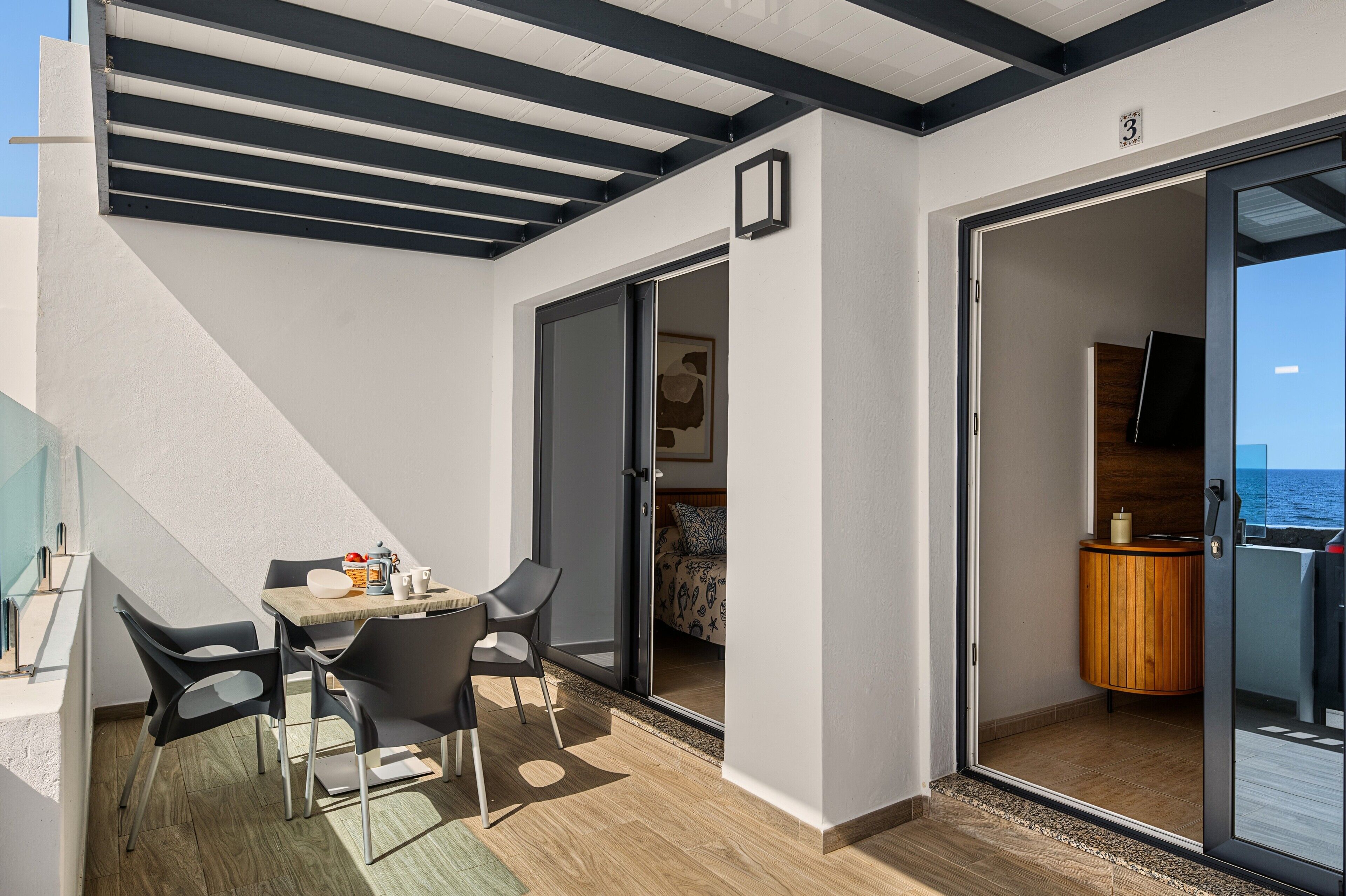Un balcón con una mesa y sillas, un armario de madera y una puerta corrediza de vidrio que da a un dormitorio.