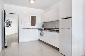 Een moderne keuken met witte kasten, een roestvrijstalen koelkast en een raam met gordijn.