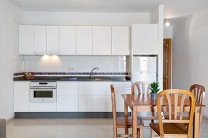 A kitchen with white cabinets, a sink, a stove, and a dining table with chairs.