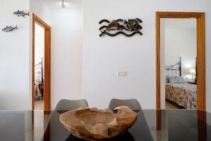 Een kamer met een houten tafel, twee stoelen, een bed met beddengoed met een patroon, een visdecoratie aan de muur en een spiegel.