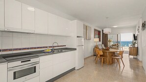 A modern kitchen with white cabinets, a black countertop, and a dining area with wooden furniture. - Holiday Apartment “Callao Beach 6” with Sea View, Terrace & Wi-Fi (Arrieta)
