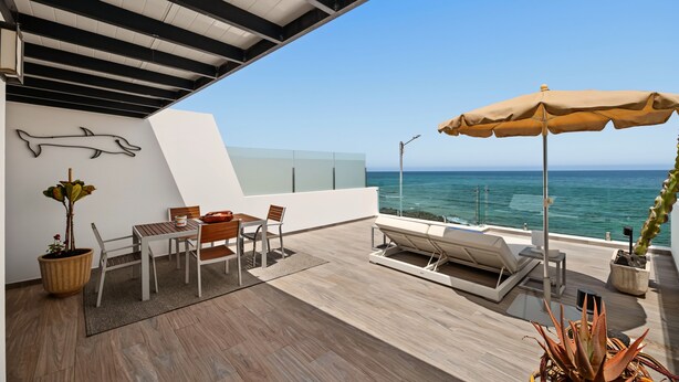 A modern outdoor seating area with a view of the sea, featuring a table, chairs, a sun lounger, and a potted plant. - Holiday Apartment “Callao Beach 6” with Sea View, Terrace & Wi-Fi (Arrieta)