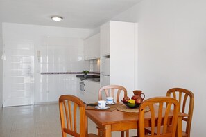 A dining area with a wooden table, four chairs, a bowl of fruit, and a white tiled backsplash.