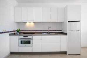 A modern kitchen with white cabinets, a stainless steel oven, a built-in sink, and a refrigerator.