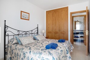 A bedroom with a bed, wooden wardrobe, and a bathroom visible through an open door.