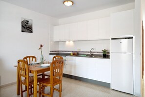 A modern kitchen with white cabinets, a stainless steel refrigerator, and a dining table with chairs. - Holiday Apartment “Callao Beach 10” with Mountain View, Terrace & Wi-Fi (Arrieta)