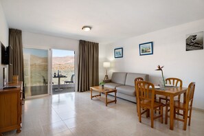 A modern living room with a sofa, dining table, chairs, a TV, and a view through a sliding door.