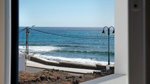 A view of the ocean through a window with a railing and street lamps.