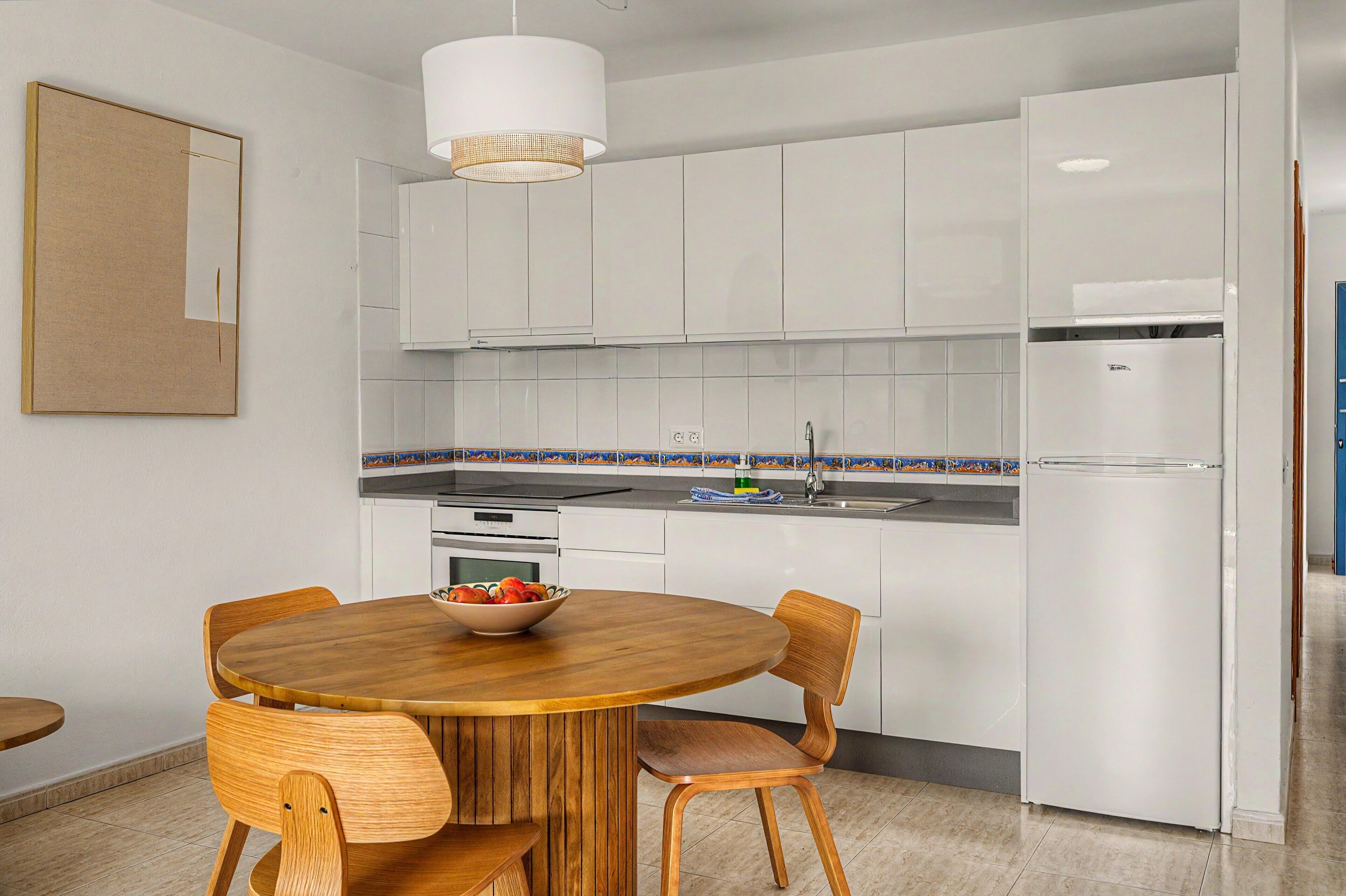 Una cocina moderna con armarios blancos, una mesa redonda de madera y sillas.