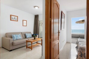 A living room with a sofa, a wooden coffee table, and a view of the sea through a window.