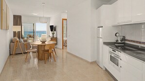 A modern kitchen with white cabinets, a dining area with a round table and chairs, and a view of the sea through large windows. - Holiday Apartment “Callao Beach 8” with Sea View, Terrace & Wi-Fi (Arrieta)