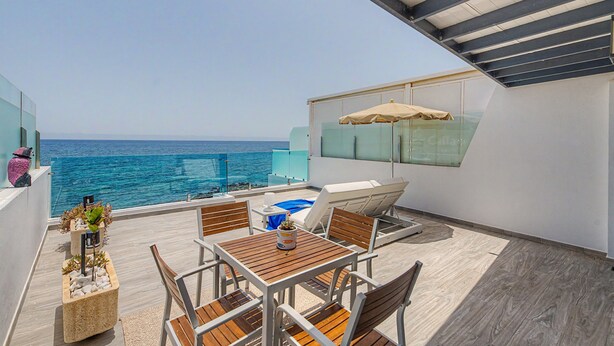 A balcony with a table, chairs, a lounge chair, and a view of the ocean. - Holiday Apartment “Callao Beach 8” with Sea View, Terrace & Wi-Fi (Arrieta)