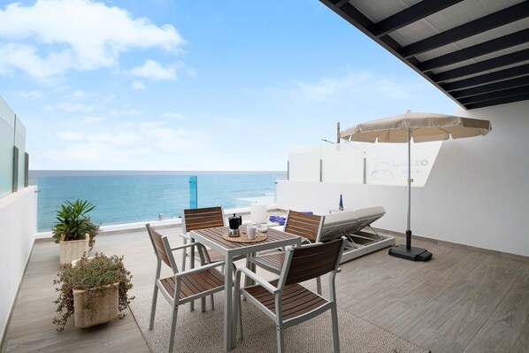 A balcony with a table, chairs, an umbrella, and potted plants.