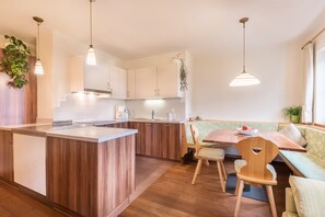 A modern kitchen with wooden cabinets, a central island, pendant lighting, and a dining area with a bench and chairs.