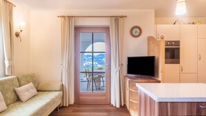 Une pièce chaleureuse avec un canapé, un téléviseur, des meubles en bois, un coin repas avec des chaises et une vue sur l’extérieur, visible à travers une porte.