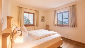 Une chambre à coucher avec un lit, deux fenêtres avec des rideaux, une lampe fixée au mur et une vue sur l’extérieur.