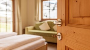 Une porte en bois avec un trou de serrure, un lit avec une literie blanche et, à l’arrière-plan, un canapé vert agrémenté de coussins blancs.