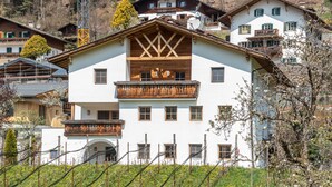 Un immeuble à plusieurs étages doté de balcons, un vignoble au premier plan et d’autres bâtiments en arrière-plan.