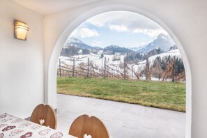 A room with a view through an arched window, a table with chairs, and a wall-mounted light.