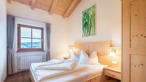 Une chambre avec un lit en bois, une fenêtre donnant sur un beau paysage, un tableau accroché au mur et une armoire en bois.