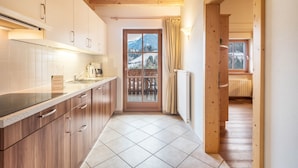 Une cuisine avec des meubles en bois, un pare-feu en carreaux et une vue sur les montagnes par une porte vitrée.