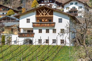 Ein mehrstöckiges Gebäude mit Balkon, ein Weinberg im Vordergrund und weitere Gebäude im Hintergrund.