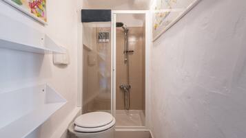 Une salle de bain comprenant des toilettes, une douche et un espace douche délimité par des parois en verre.