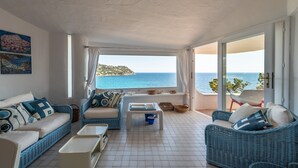 Una habitación con balcón, muebles de mimbre, suelo de baldosas y vista al mar.