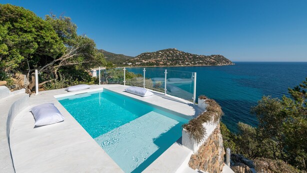 Una piscina infinita moderna con vista despejada al mar y a una isla montañosa.