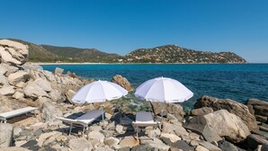 Una playa rocosa con sombrillas y sillas de playa blancas.