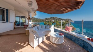 Un espacio de estar al aire libre cubierto, con vista al mar y a las colinas.