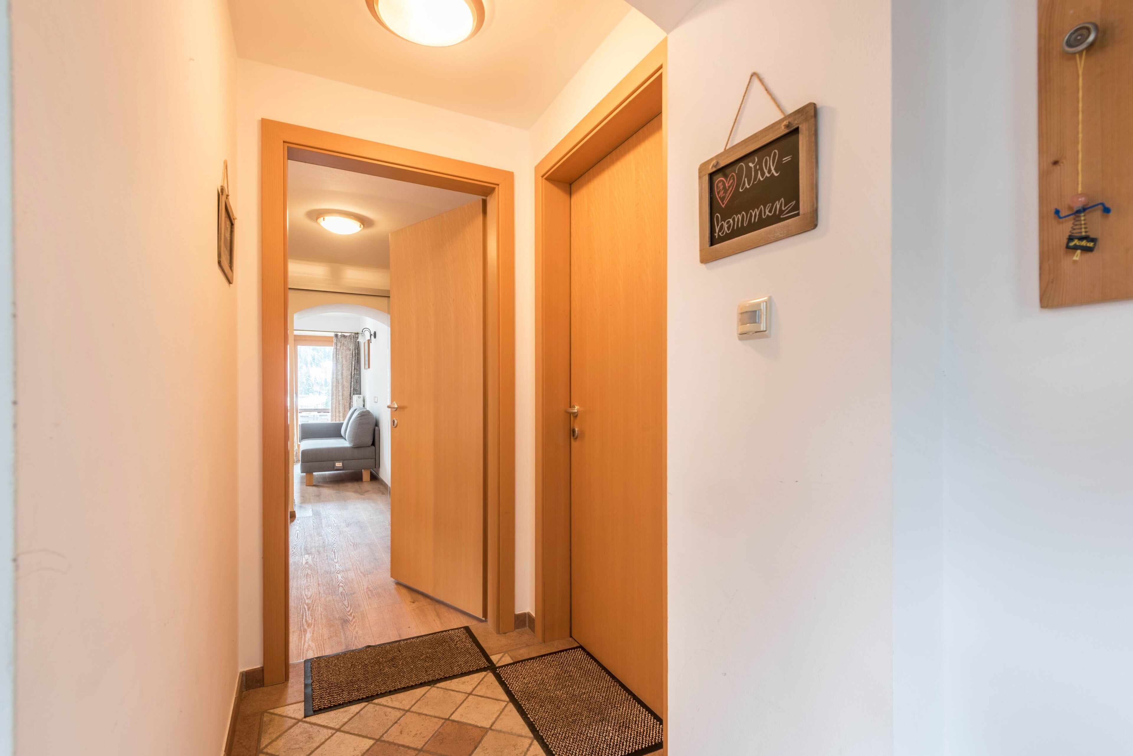 A hallway with wooden doors, a doormat, and a sign on the wall.