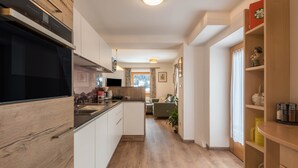 A modern kitchen with wooden cabinets, a built-in oven, and a dining area with a table and chairs. - Homely Apartment “Santner Villa Erna” with Mountain View (Seis)