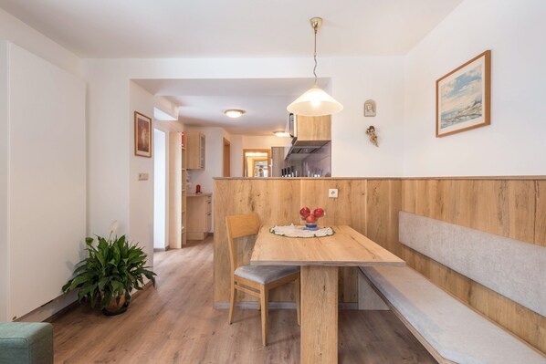 A dining area with a wooden table, chairs, a bench, a hanging light fixture, and a potted plant.