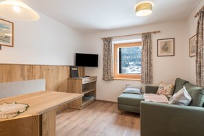 A cozy room with a wooden desk, a green sofa, a television, and a window with curtains.