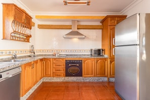 Una cocina con armarios de madera, un refrigerador de acero inoxidable, un lavavajillas y un horno empotrado.