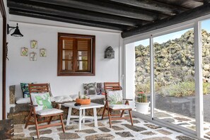 A room with a stone floor, wooden furniture, a window with a view of rocks, and cactus-themed decor. - Vacation Home “Casa Vereda del Risco” with Sea View, Mountain View & Garden (Yé)