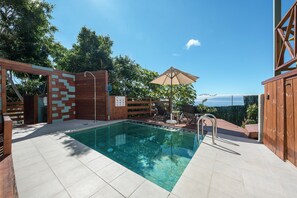 Una piscina con cubierta de madera, un pérgola y vista al mar.